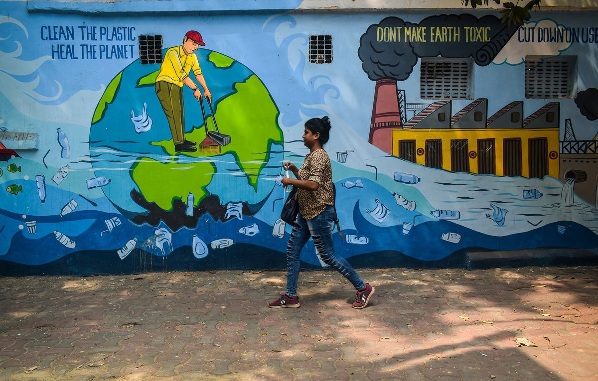 A woman walks past a mural depicting Pollution caused by