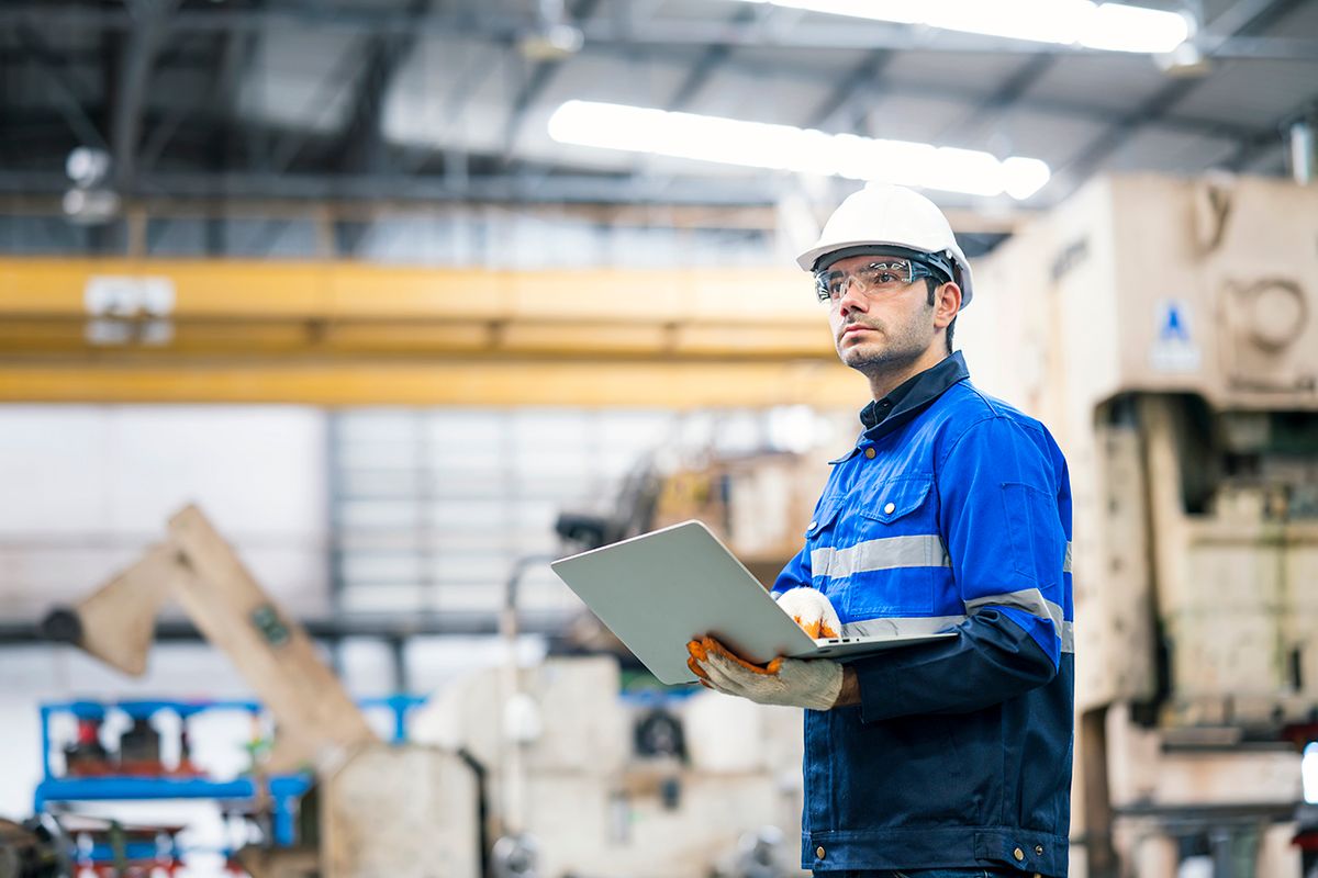 Auto part production in the automobile industry. Portrait of a production line surveyor engineer working at a large hydraulic stamping press machine and holding a laptop. He expert in planning, improvement, and monitoring of the production processes. Auto part production in the automobile industry. Portrait of a production line surveyor engineer working at a large hydraulic stamping press machine and holding a laptop. He expert in planning, improvement, and monitoring of the production processes.