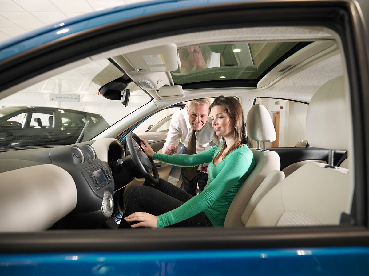 Salesman advises female customer who is sat in car in car dealership