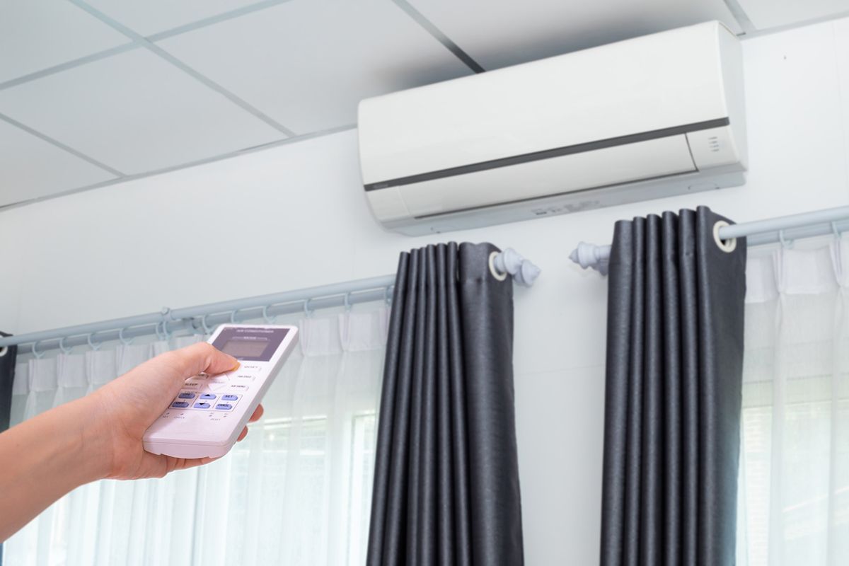 Cropped Hand Of Woman Holding Air Conditioner Remoter Human hand controling air conditioner in room.
