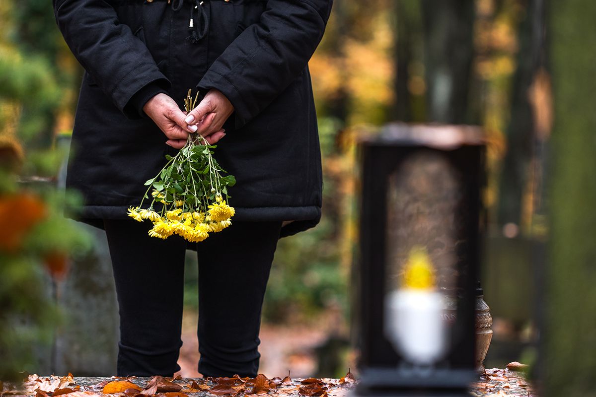 Mourning,Woman,Holding,Flowers,In,Hands,And,Standing,At,Grave
Mourning woman holding flowers in hands and standing at grave in cemetery. Sadness during funeral