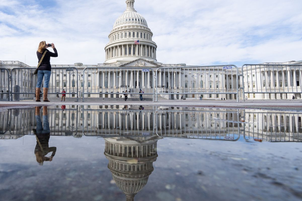 UNITED STATES - FEBRUARY 13: A tourist is reflected in a rain puddle as she stops to stake a photo of the U.S. Capitol in Washington on Monday, February 13, 2023. 