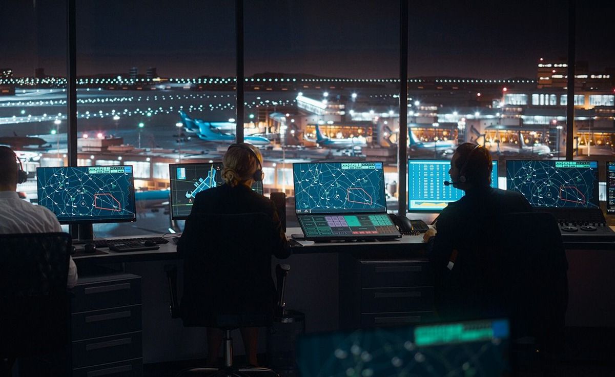 Diverse Air Traffic Control Team Working in a Modern Airport Tower at Night. Office Room is Full of Desktop Computer Displays with Navigation Screens, Airplane Flight Radar Data for Controllers. Diverse Air Traffic Control Team Working in a Modern Airport Tower at Night. Office Room is Full of Desktop Computer Displays with Navigation Screens, Airplane Flight Radar Data for Controllers.