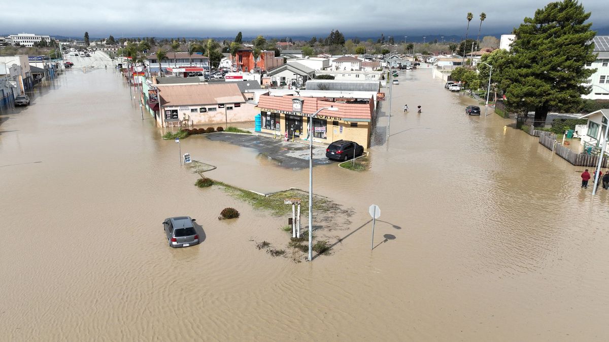 An aerial view shows people wading through a flooded neighborhood in the unincorporated community of Pajaro in Watsonville, California, on March 11, 2023. - Residents were forced to evacuate in the middle of the night after an atmospheric river surge broke the Pajaro Levee and sent flood waters flowing into the community. 