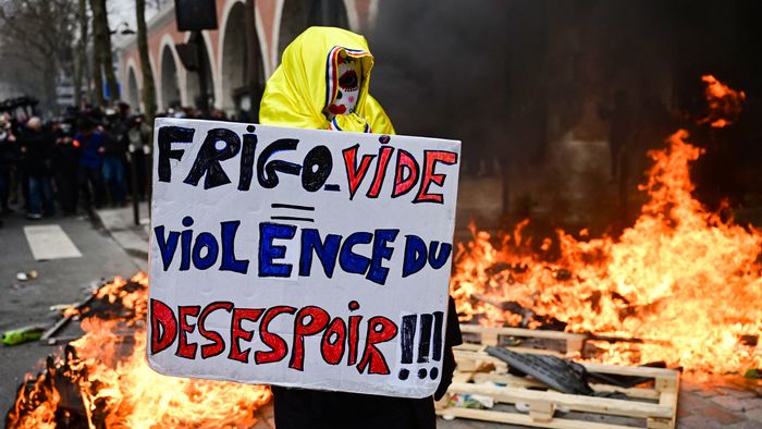A protestor holds a placard which reads "Empty Fridge equals Violence of Dispair" in front of a pile of burning rubbish on the sidelines of a demonstration as part of a nationwide day of strikes and protests called by unions over the proposed pensions overhaul, in Paris on March 11, 2023. - The reform proposed by the government includes the raise of the minimum retirement age from 62 to 64 years and the increase of the number of years people have to make contributions for a full pension. Unions have vowed to keep up the pressure on the government, with a seventh day of mass protests, and some have even said they would keep up rolling indefinite strikes. (Photo by Emmanuel DUNAND / AFP)