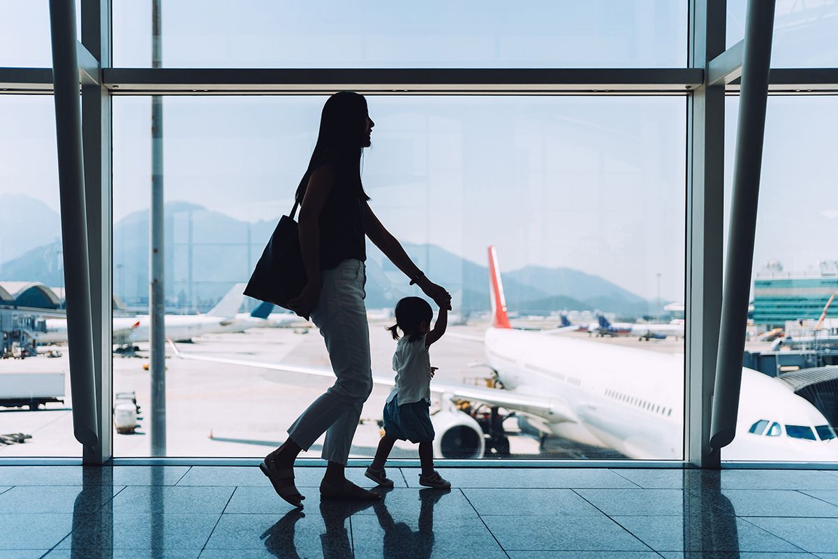 UTAZÁS
Silhouette of joyful young Asian mother holding hands of cute little daughter looking at airplane through window at the airport while waiting for departure