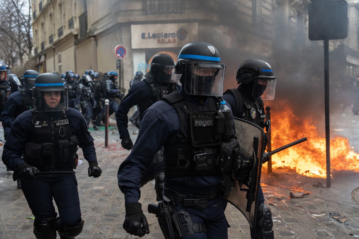 PARIS, FRANCE - MARCH 28: Police officers pass by a fire as they charge protesters during a rally against pension reforms on March 28, 2023 in Paris, France. The country has experienced weeks of protests and strike actions related to a rise in the pension age, which was passed last week. The 10th day of nationwide protests in France against the pension reforms are also calling out the police brutality from pervious strikes. 