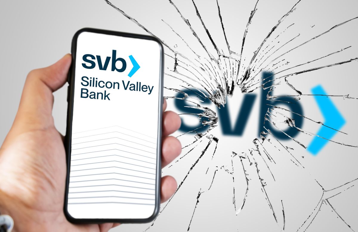 Santa Clara, USA, March 2023: Hand holding a phone with Silicon Valley Bank website on the screen with broken glass and blurred SVB logo in the background. Bank run and bankruptcy.