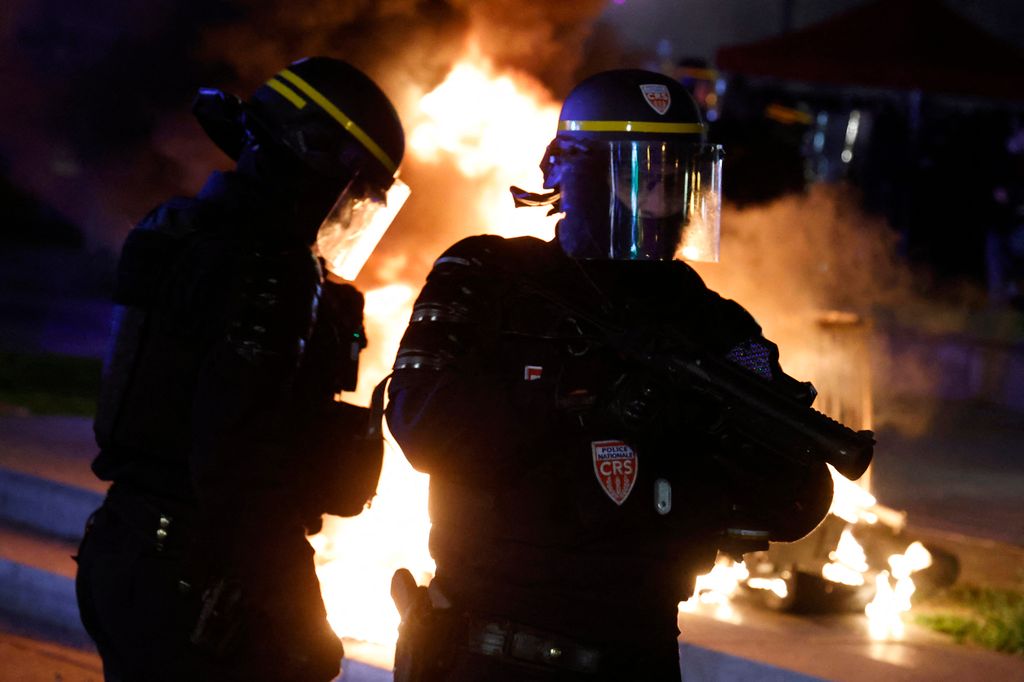 A CRS riot police officer holds a rubber defensive bullet launcher (LBD 40) next to a fire set by protesters at Place de la Republique during a demonstration, a few days after the government pushed a pensions reform through parliament without a vote, using the article 49.3 of the constitution, in Paris on March 21, 2023. - French Prime Minister's government on March 20, 2023 narrowly survived the first -- and more risky -- of two no-confidence motions over its decision to bypass parliament and impose a controversial pension reform. French President told allies he plans to keep the government in place and not dissolve parliament, defying opponents and widespread public anger over his pensions reform. (Photo by Ludovic MARIN / AFP)