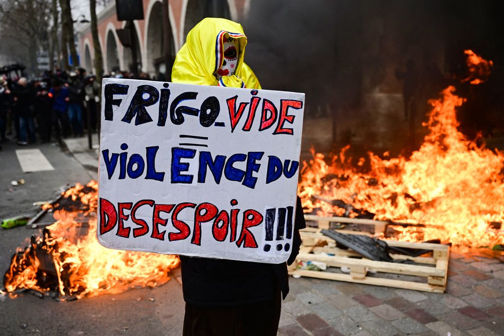 A protestor holds a placard which reads "Empty Fridge equals Violence of Dispair" in front of a pile of burning rubbish on the sidelines of a demonstration as part of a nationwide day of strikes and protests called by unions over the proposed pensions overhaul, in Paris on March 11, 2023. - The reform proposed by the government includes the raise of the minimum retirement age from 62 to 64 years and the increase of the number of years people have to make contributions for a full pension. Unions have vowed to keep up the pressure on the government, with a seventh day of mass protests, and some have even said they would keep up rolling indefinite strikes. (Photo by Emmanuel DUNAND / AFP)