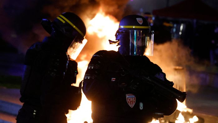 A CRS riot police officer holds a rubber defensive bullet launcher (LBD 40) next to a fire set by protesters at Place de la Republique during a demonstration, a few days after the government pushed a pensions reform through parliament without a vote, using the article 49.3 of the constitution, in Paris on March 21, 2023. - French Prime Minister's government on March 20, 2023 narrowly survived the first -- and more risky -- of two no-confidence motions over its decision to bypass parliament and impose a controversial pension reform. French President told allies he plans to keep the government in place and not dissolve parliament, defying opponents and widespread public anger over his pensions reform. (Photo by Ludovic MARIN / AFP)