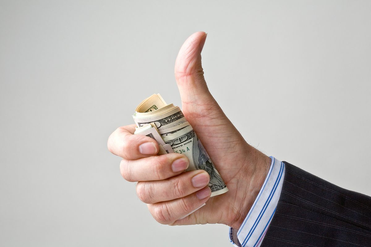 financial thumbs up for US dollar.
businessman's hand grips dollar and gives thumbs up gesture