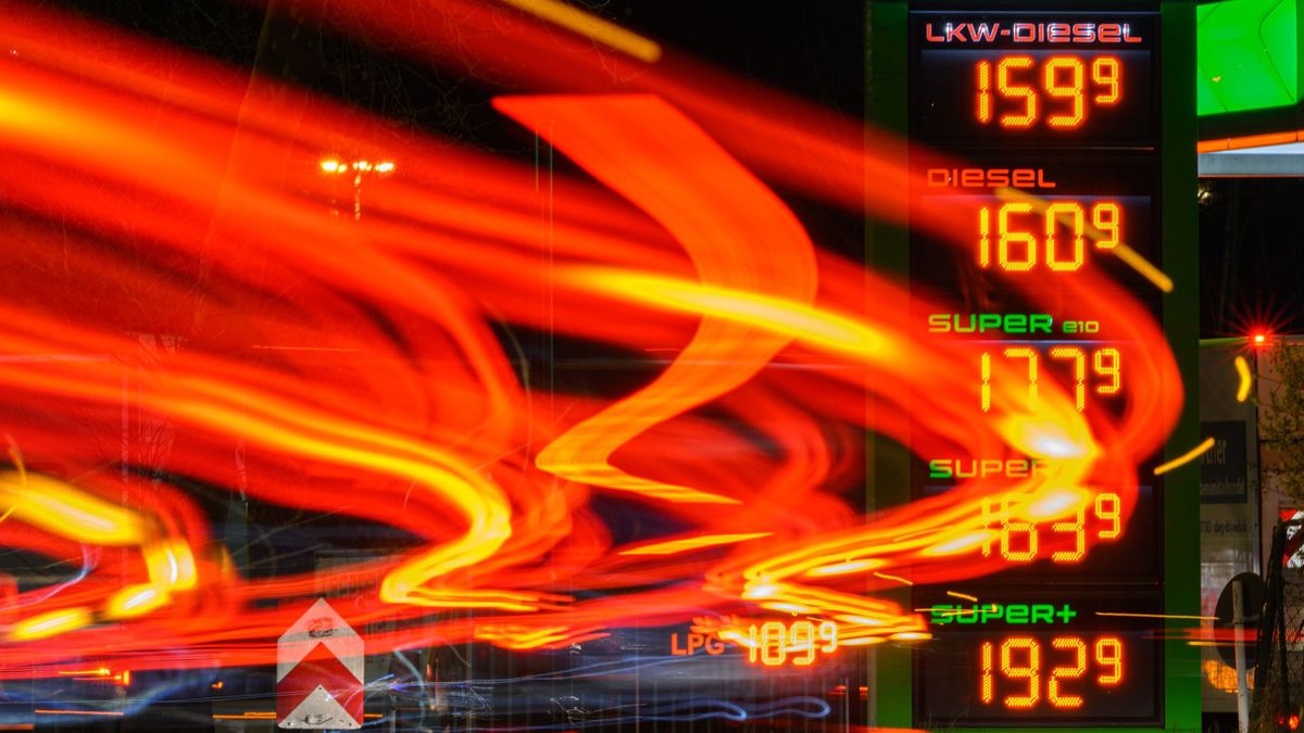 Gasoline pric04 April 2023, Saxony, Dresden: The headlights of passing vehicles draw light trails on a street in the morning while in the background the price board of a gas station shows the gasoline prices. (shot with long exposure time) 
