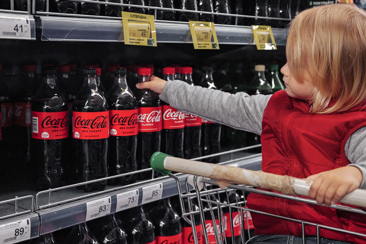 St,Petersburg,,Russia,,August,2021:,Adorable,Toddler,Girl,Sitting,In St Petersburg, Russia, august 2021: Adorable toddler girl sitting in shopping cart buying coca-cola on a store shelf. Portrait little cute kid going shopping  in store or supermarket