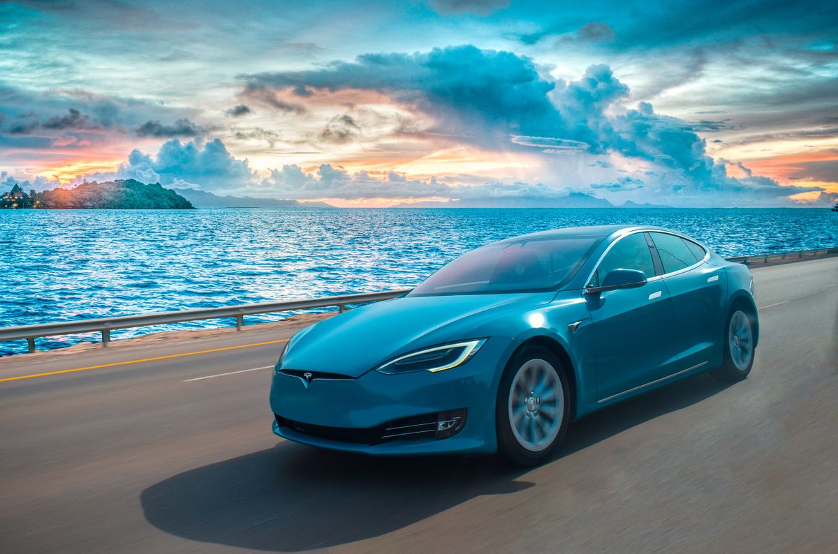 Abudhabi,UAE on 27-11-2018.A rare blue coloured tesla model s drives on a beach side abudhabi road.There is a sunset behind the ocean.