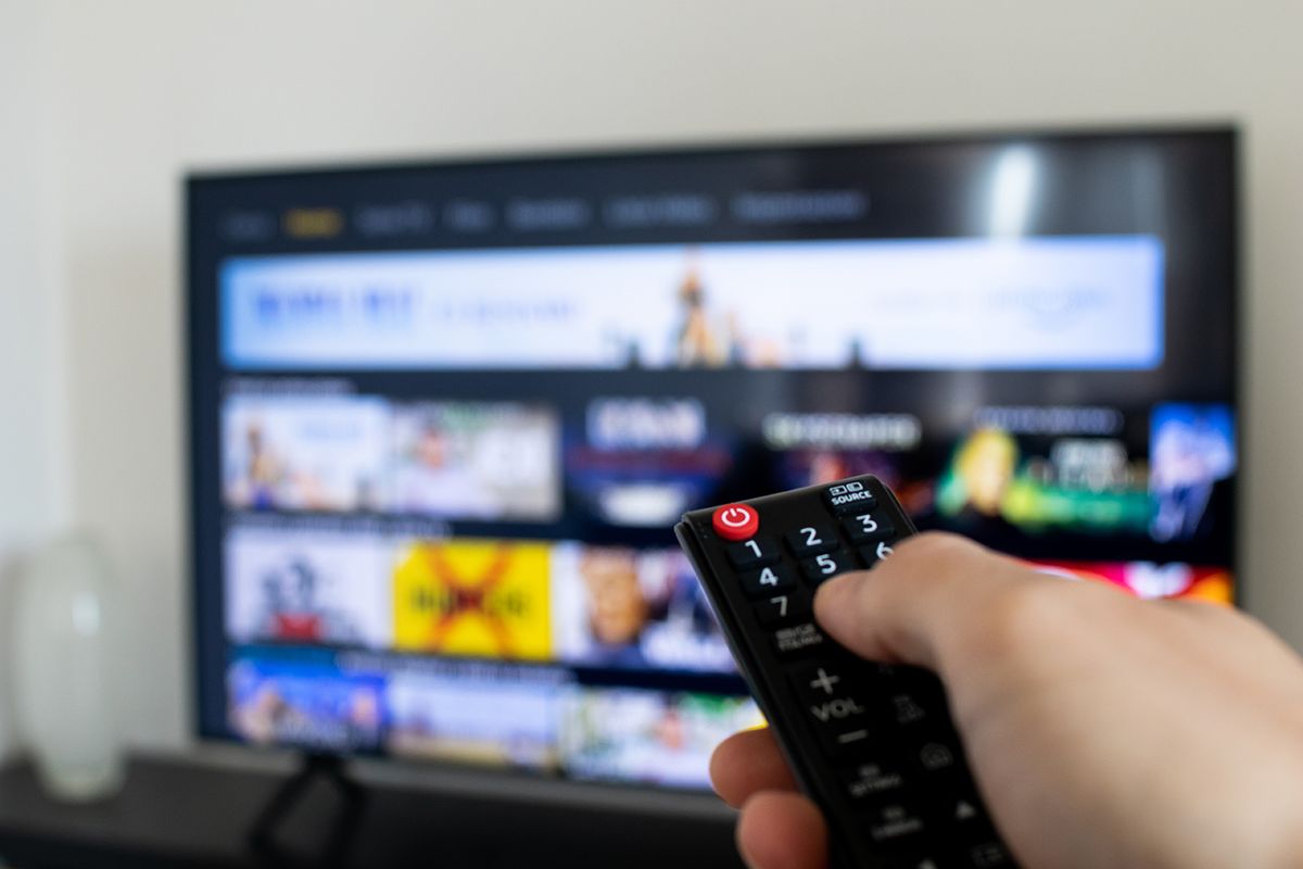 Tv,Remote,Controller,In,Hand,Of,Customer,Looking,For,Some
Tv remote controller in hand of customer looking for some content in Smart Tv app for streaming video. Watching streaming services for entertainment on television. Choosing TV series and movies