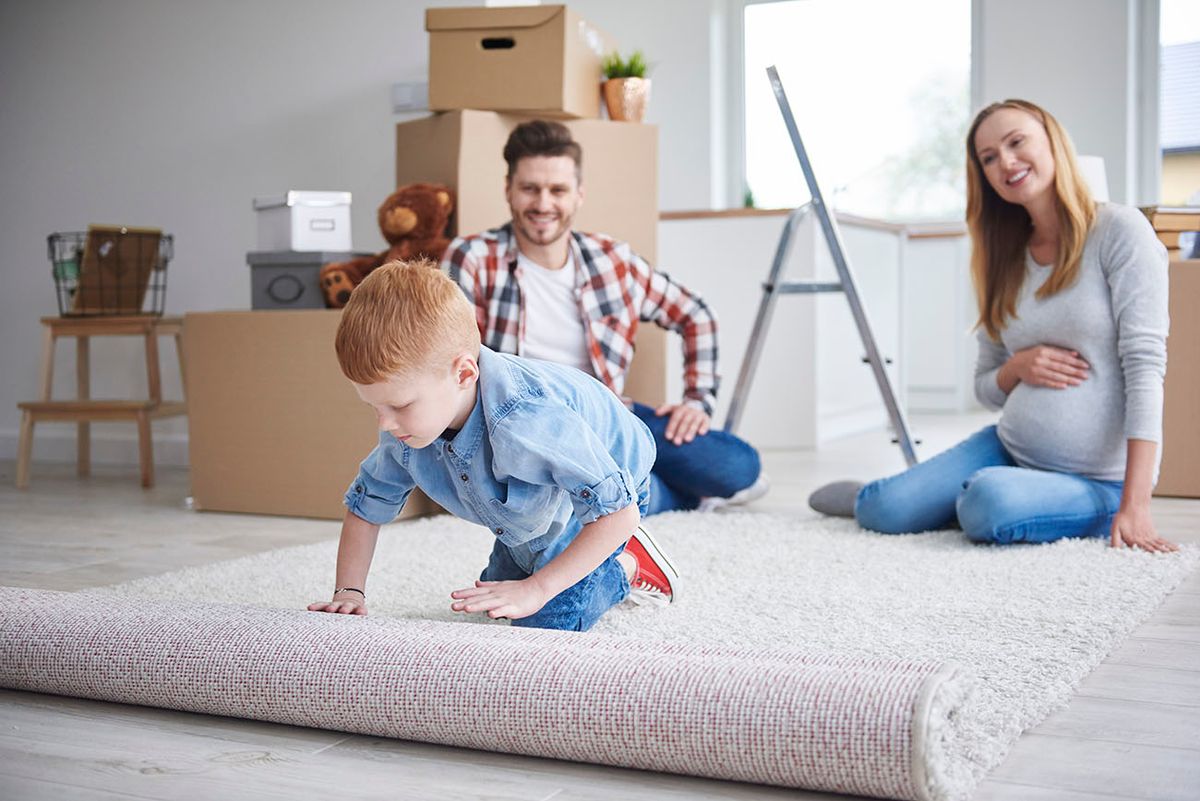 Boy with parents unrolling a carpet in new flat