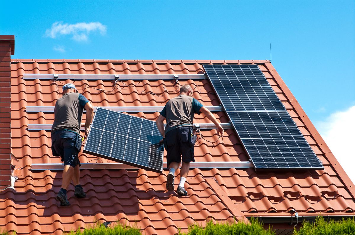 Two,Men,Installing,New,Solar,Panels,On,The,Roof,Of Two men installing new solar panels on the roof of a private house. Renewable energy concept and green energy abstract.