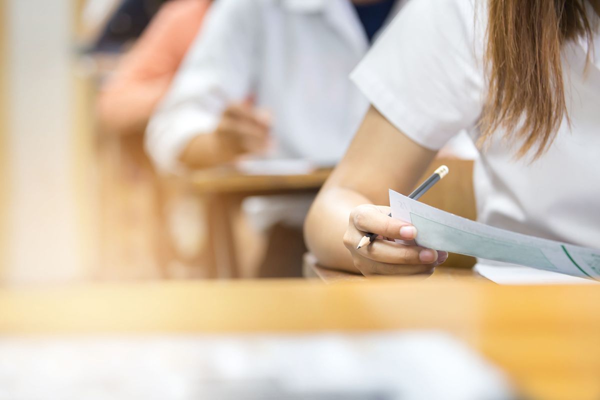soft focus.hand high school or university student in uniform holding pencil writing on paper answer sheet.sitting on lecture chair taking final exam or study attending in examination room or classroom