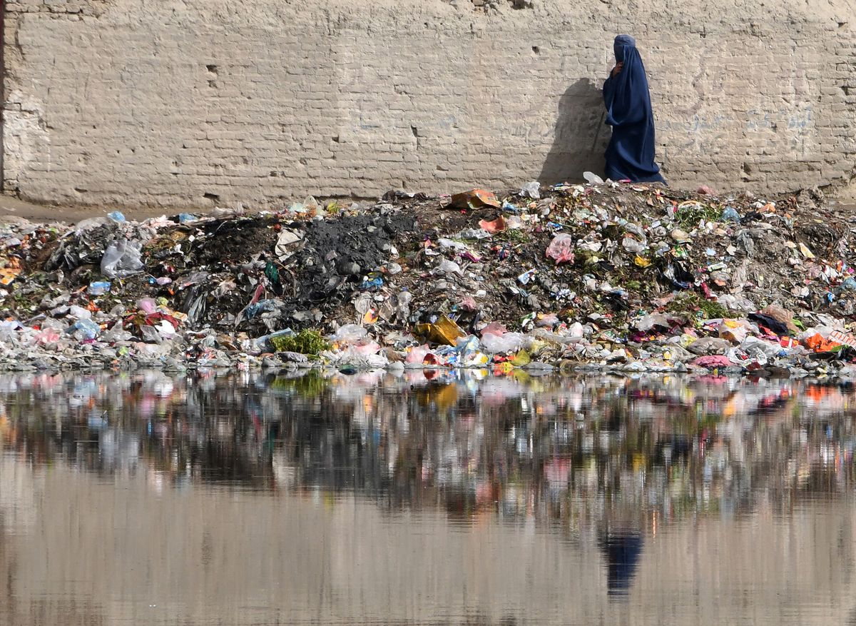 (FILES) An Afghan woman walks next to a pile of trash full of plastic bags in Kabul on May 6, 2018. Negotiations on a global treaty to combat plastic pollution will resume on May 29, 2023, with nations under pressure to stem the tide of trash amid calls from campaigners to limit industry influence on the talks. Some 175 nations pledged last year to agree by 2024 a binding deal to end the pollution from largely fossil fuel-based plastics that is choking the environment and infiltrating the bodies of humans and animals. The May 29-June 2 talks in Paris are tasked with agreeing the first outline for actions that could form the basis of a draft negotiating text.