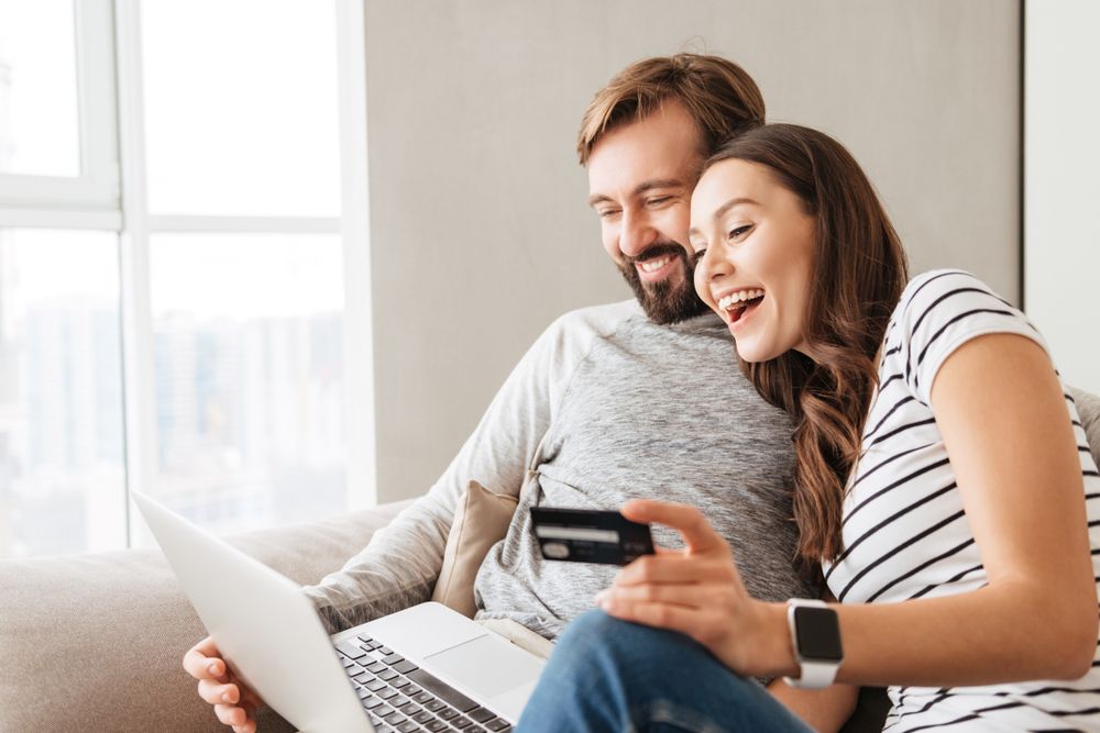 Portrait,Of,A,Laughing,Young,Couple,Shopping,Online,While,Sitting