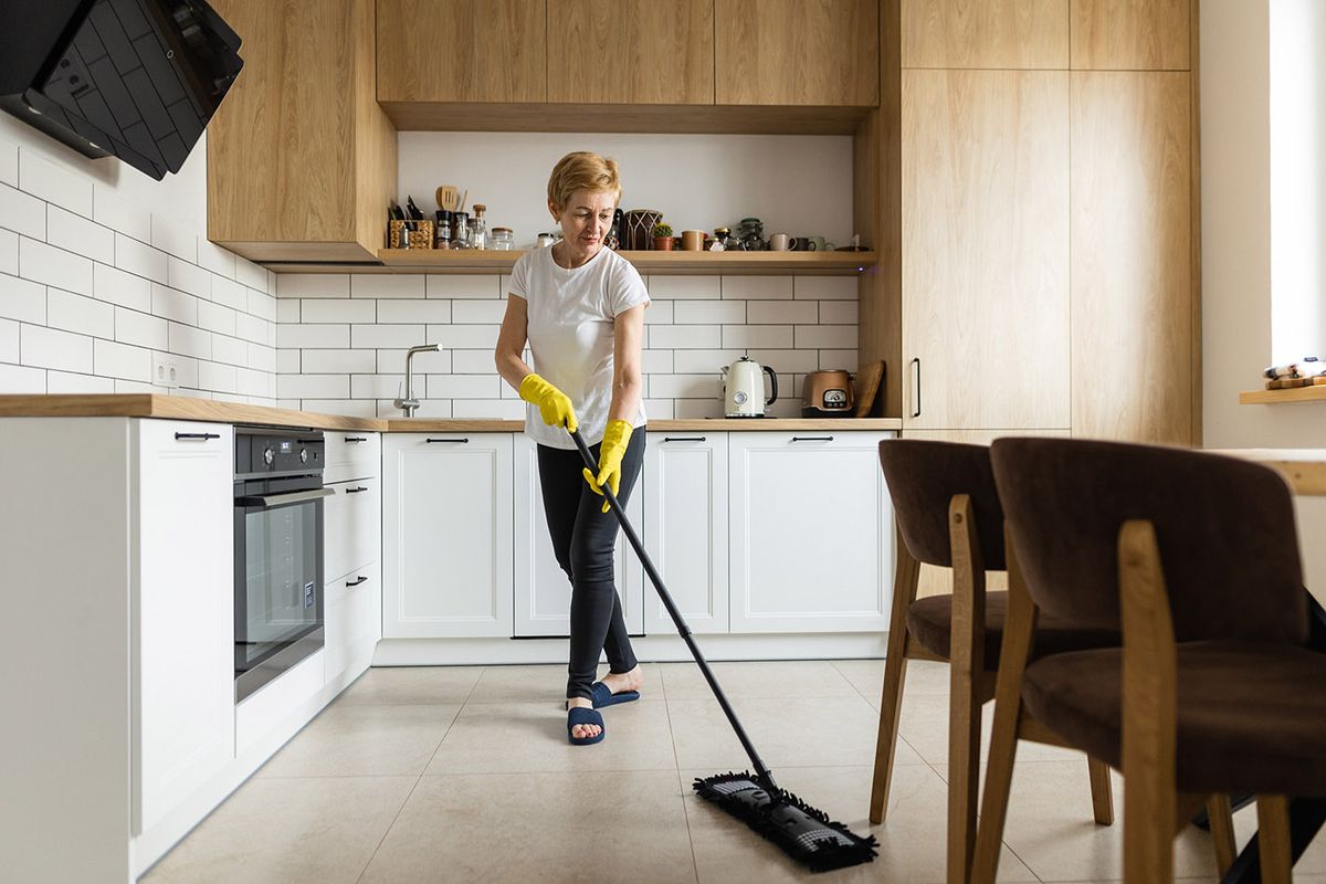 The mature woman washes the floor in the kitchen using a mop
The mature housewife using the chenille mop to clean the floor in the kitchen at home