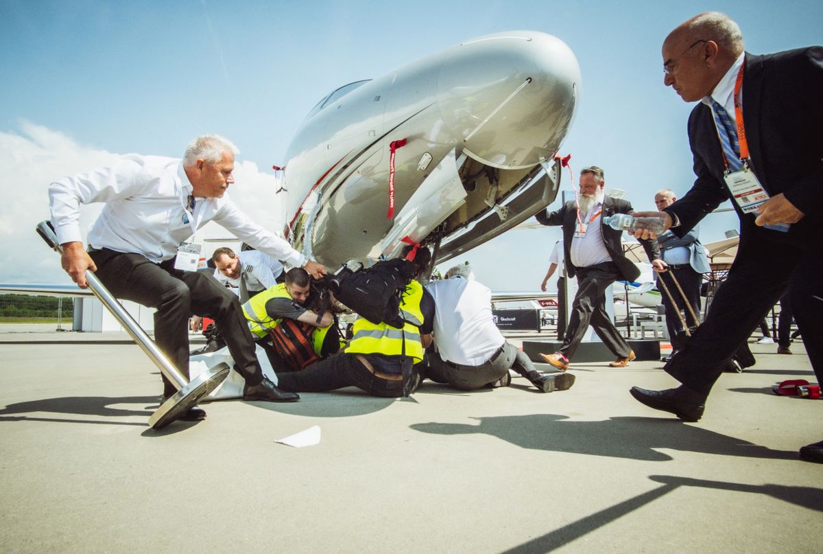 This handout picture taken and released on May 23, 2023 by Greenpeace shows unidentified people rushing to climate activists beneath a business jet during a protest at European business aviation show EBACE (European Business Aviation Convention & Exhibition) at Geneva Airport on May 23, 2023. Protesters on the tarmac at Geneva airport briefly disrupted air traffic before operations were gradually resumed, the airport said, as dozens of climate activists blocked a nearby business jet convention. 