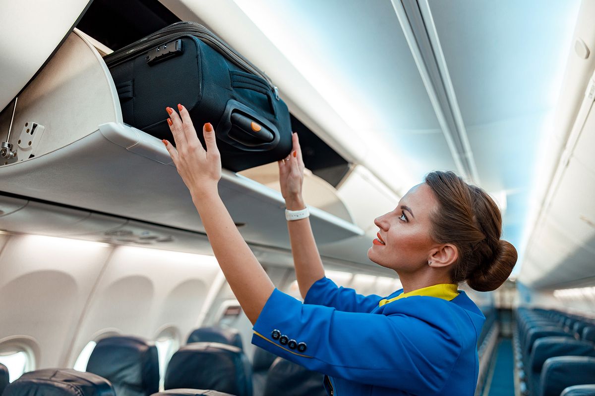 Woman,Flight,Attendant,Or,Air,Hostess,Placing,Travel,Bag,In
Woman flight attendant or air hostess placing travel bag in overhead baggage locker while standing in airplane passenger salon