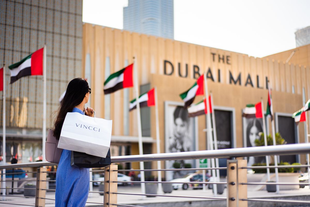 Dubai, United Arab Emirates - March 26, 2018: Asian tourist in front of Dubai mall main entrance with shopping bags
