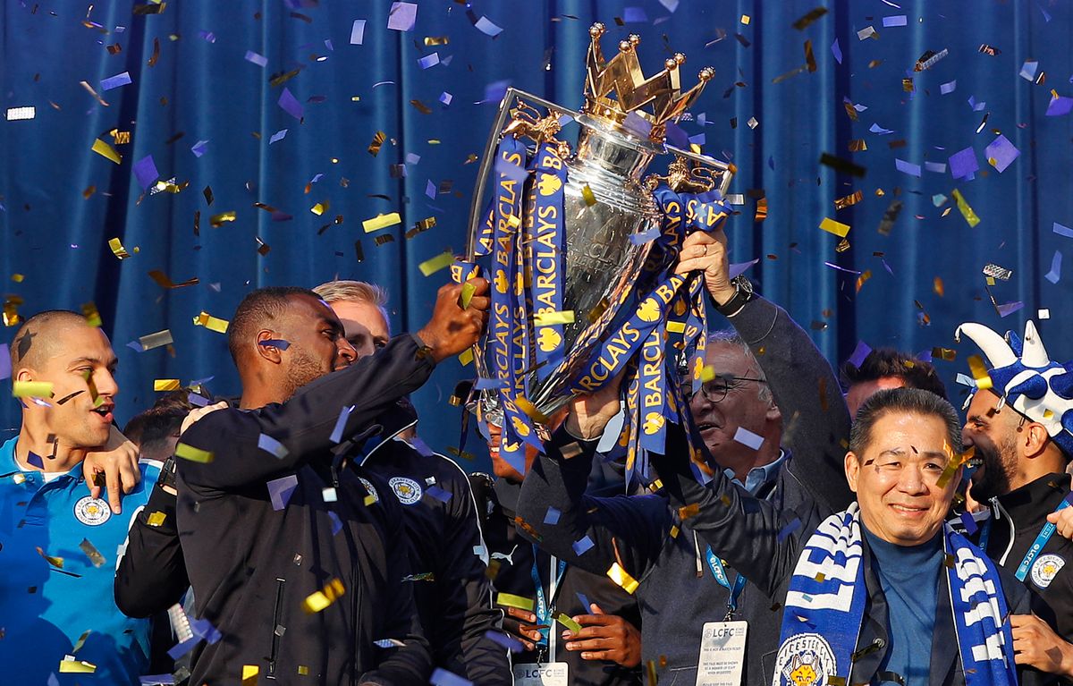 Leicester City's Thai owner and chairman Vichai Srivaddhanaprabha (R), Leicester City's Italian manager Claudio Ranieri (2R) and Leicester City's English defender Wes Morgan (2L) hold up the Premier league trophy to fans as the Leicester City team celebrate in Victoria Park, after taking part in an open-top bus parade through Leicester, to celebrate winning the Premier League title on May 16, 2016. (Photo by ADRIAN DENNIS / AFP)