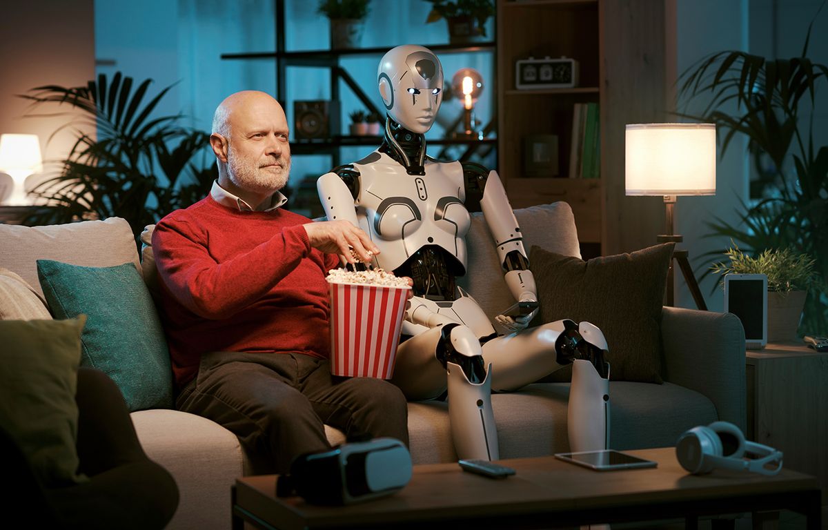 Senior man and female AI robot sitting on the couch at home, they are watching movies together, human-robot relationship concept