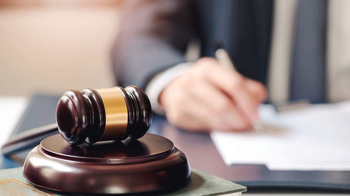 Closeup,Judge,Wooden,Gavel,On,Sounding,Block,With,Blur,Image
Closeup judge wooden gavel on sounding block with blur image of man hand writing on background.