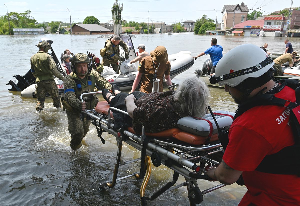 Ukrainian servicemen help to unload a disabled local resident from a boat during an evacuation from a flooded area in Kherson on June 8, 2023, following damages sustained at Kakhovka hydroelectric power plant dam. Ukraine and Russia accused each other of shelling in the flood-hit Kherson region on June 8, 2023 even as rescuers raced to save people stranded after the destruction of a Russian-held dam unleashed a torrent of water. (Photo by Genya SAVILOV / AFP)