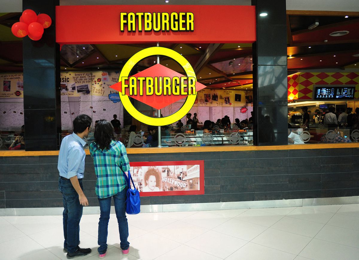 TO GO WITH "Pakistan-unrest-economy-consumerism,FEATURE" by Hasan MansoorIn this picture taken on January 10, 2013 Pakistani pedestrians stand outside a Fatburger outlet in Karachi. American fast-food and Western fashion outlets are taking Pakistan's growing middle class by storm, defying stereotypes about a conservative Muslim country gripped by Al-Qaeda and the Taliban.  AFP PHOTO/Rizwan TABASSUM (Photo by RIZWAN TABASSUM / AFP)