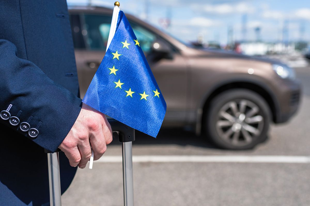 Man,In,A,Blue,Suit,With,A,Suitcase,And,Europe
Man in a blue suit with a suitcase and Europe or European(EU)  flag at the airport parking on the backdrop of his car. Business trip concept