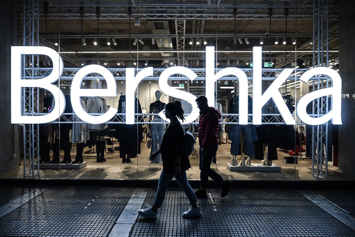 Pedestrians walk next to a lighted Bershka logo and shop in Thessaloniki on October 5, 2022. The Thessaloniki Chamber of Commerce proposed to reduced store opening hours during the afternoon and evening hours as a “weapon” of defense against the energy “war” that is denied that they would take such general measures on October 5, 2022. Instead, it would  let local commerce unions decide on the stores working hours. (Photo by Sakis MITROLIDIS / AFP)