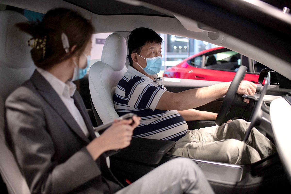 CHINA-ECONOMY-TESLAA man (R) sits inside of a Tesla car Model 3 as a vendor talks to him at a Tesla shop inside of a shopping Mall in Beijing on May 26, 2021. (Photo by NICOLAS ASFOURI / AFP)