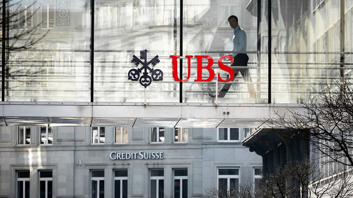A employee is seen in silhouette next to a sign of Swiss giant banking UBS and a sign of Credit Suisse bank in Zurich on March 20, 2023. UBS share price plunged on March 20, 2023 as a deal to take over its troubled Swiss rival Credit Suisse for $3.25 billion failed to calm stock market nerves. (Photo by Fabrice COFFRINI / AFP)