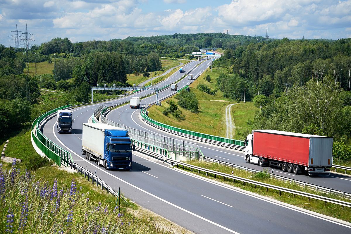 View,From,Above,Of,Trucks,Driving,On,The,Highway,With
View from above of trucks driving on the highway with electronic toll gates in a wooded landscape.