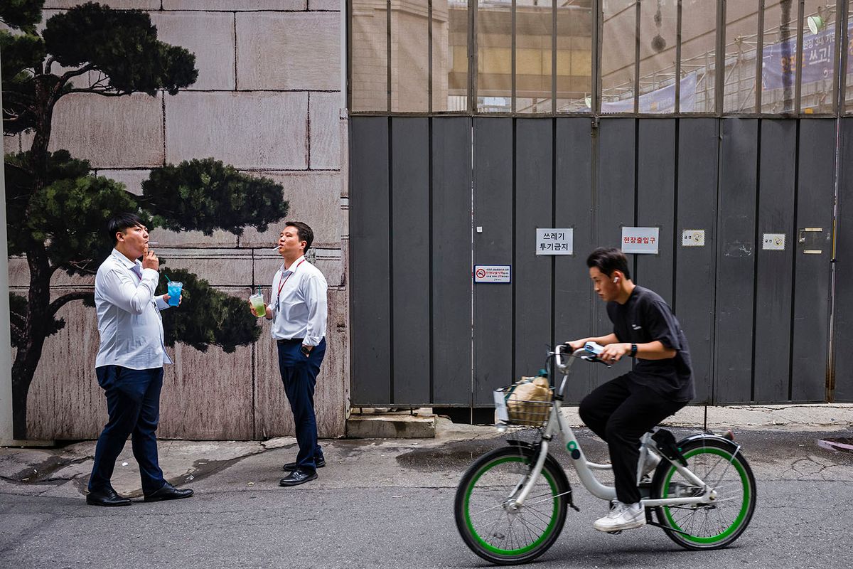 SKOREA-LIFESTYLE
A cyclist rides past two men smoking cigarettes in Seoul on June 20, 2023. (Photo by ANTHONY WALLACE / AFP)