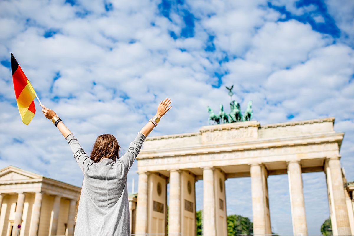 Young,Woman,Tourist,Standing,Back,With,Raised,Hands,And,German