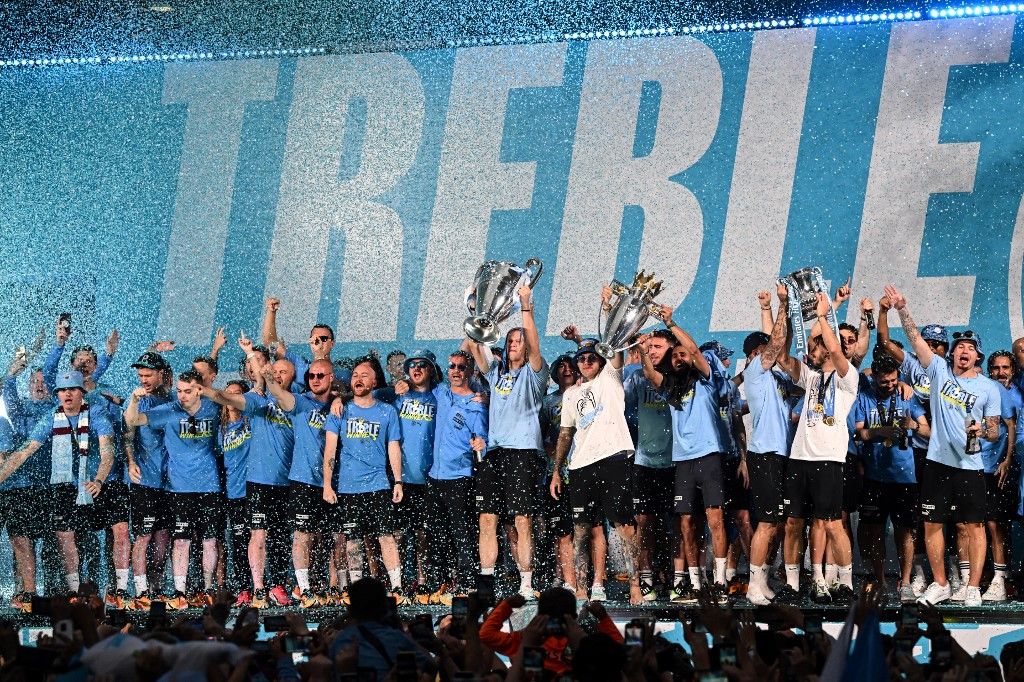 Manchester City's players celebrate on stage with their trophies following an open-top bus victory parade for their European Cup, FA Cup and Premier League victories, in Manchester, northern England on June 12, 2023. Manchester City tasted Champions League glory at last on Saturday as a second-half Rodri strike gave the favourites a 1-0 victory over Inter Milan in a tense final, allowing Pep Guardiola's side to complete a remarkable treble. Having already claimed a fifth Premier League title in six seasons, and added the FA Cup, City are the first English club to win such a treble since Manchester United in 1999. (Photo by Oli SCARFF / AFP)