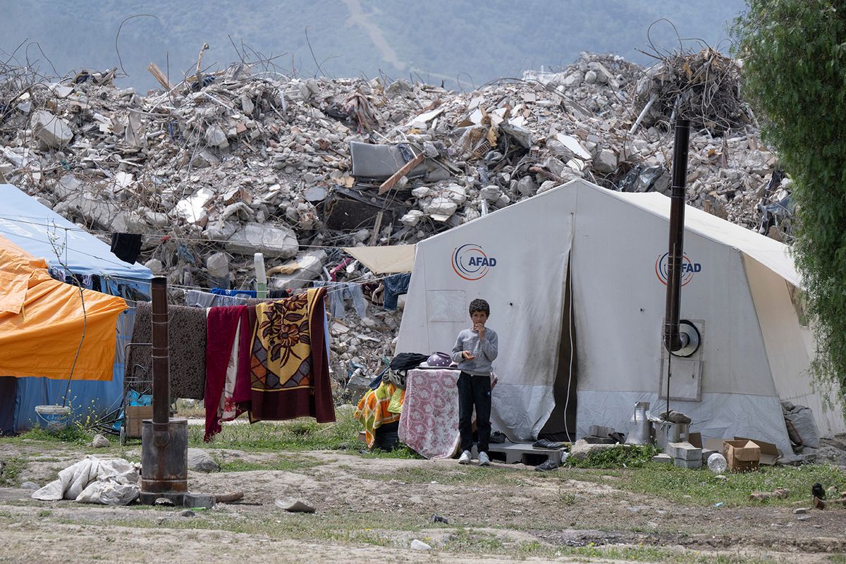 Turkey after the earthquake - Antakya27 April 2023, Turkey, Antakya: Nine-year-old Yakup stands on the outskirts of Antakya in front of his tent, where he has been living since the earthquake. Behind him, mountains of rubble pile up from the rubble of destroyed houses. Large parts of the city were completely destroyed in the earthquake on February 6. Photo: Boris Roessler/dpa Turkey After The Earthquake April  , 2023
