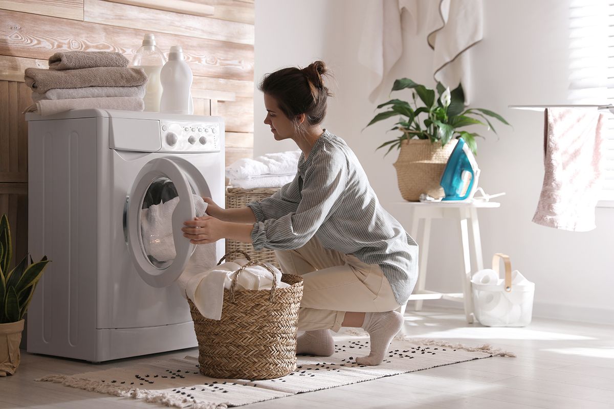 Young,Woman,Taking,Laundry,Out,Of,Washing,Machine,At,Home