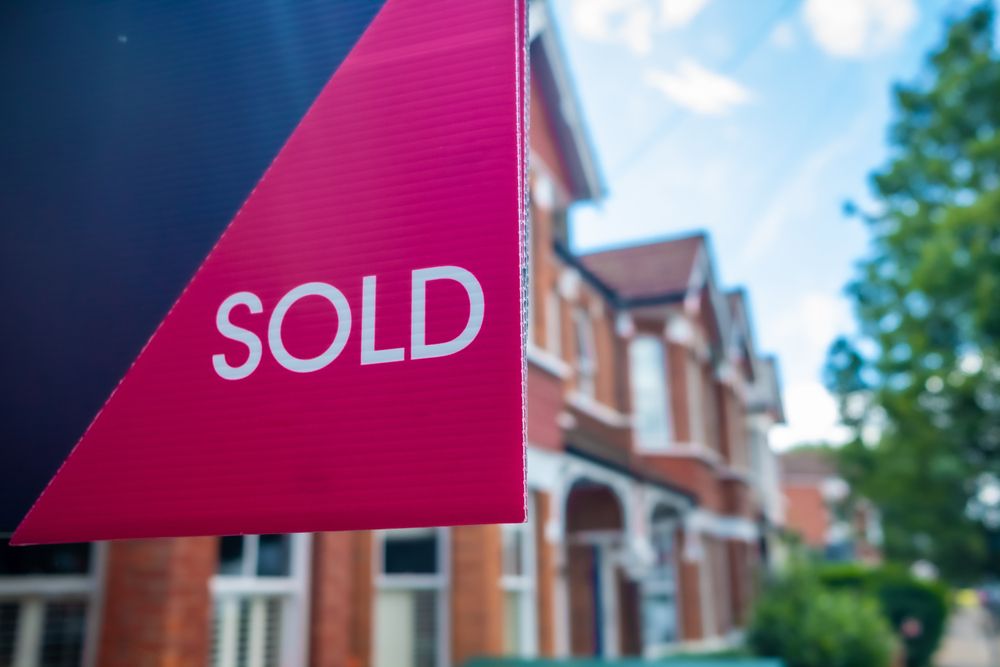 Estate,Agent,Sold,Sign,With,Defocussed,Street,Of,Houses,In