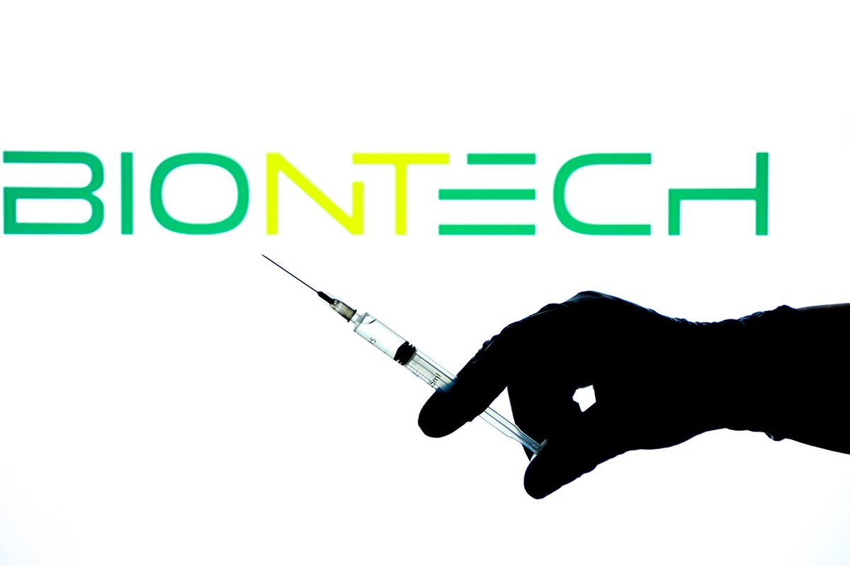 Madrid, Spain- May 2, 2021: Hand on surgery glove holding Syringe with Covid vaccine. In the background Biontech Laboratory logo
