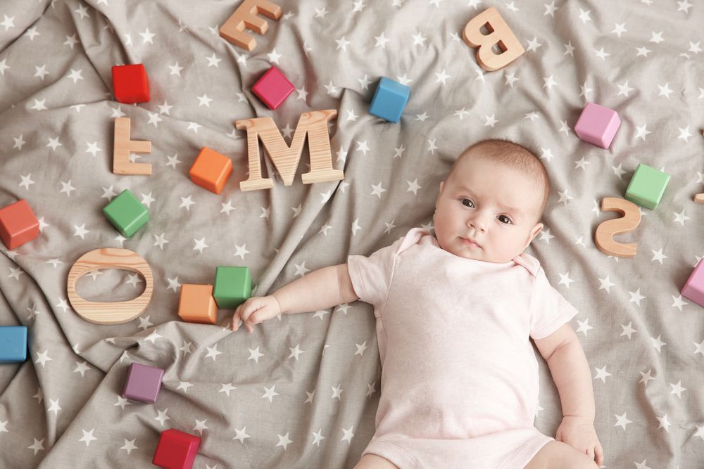 Cute,Baby,With,Different,Letters,And,Cubes,Lying,On,Bed.