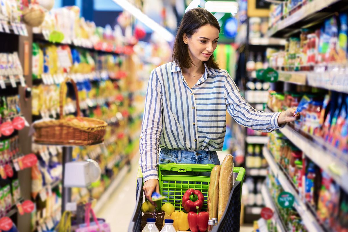 At,The,Supermarket.,Portrait,Of,Young,Woman,Standing,With,Trolley
At The Supermarket. Portrait Of Young Woman Standing With Trolley Cart Between Aisles In Grocery Store. Cheerful Consumer Buying Essentials In Local Shop, Taking Products From Shelf