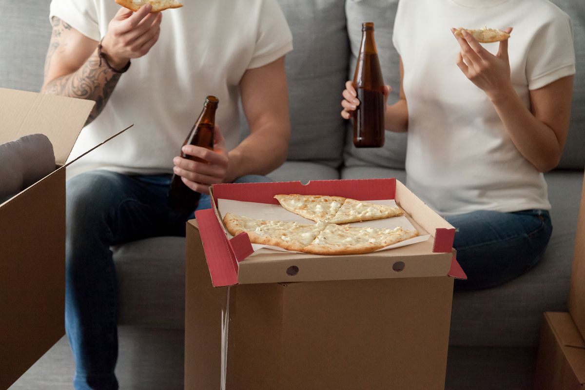 Couple,Eating,Pizza,Celebrating,Housewarming,Party,On,Moving,Day,,Man
Couple eating pizza celebrating housewarming party on moving day, man and woman enjoying beer and snack sitting on sofa with unpacked boxes around, move in new home, delivery service, close up view