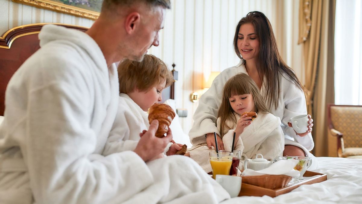 Close,Up,Of,Parents,And,Two,Kids,In,White,Bathrobes
Close up of parents and two kids in white bathrobes having breakfast in bed, eating and drinking in luxurious hotel room. Family, resort, room service concept. Horizontal shot. Selective focus